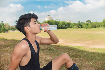 A young asian man quenches his thirst with a water bottle. Relaxing after an outdoor cardio workout.