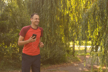 A handsome man in a T-shirt trains in the park and listens to music on headphones
