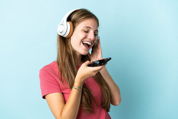 Young caucasian woman isolated on blue background listening music with a mobile and singing