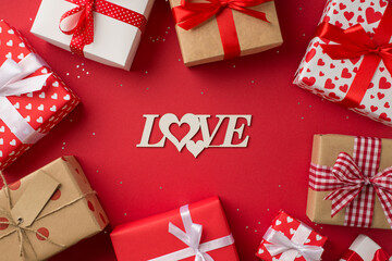Top view photo of st valentine's day decorations inscription love in the middle gift boxes and sequins on isolated red background