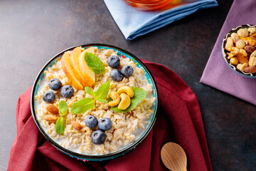 Oatmeal porridge with yogurt, berries and nuts on burgundy napkin. Bowl with oatmeal, blueberries, apples and honey on a dark background. Healthy breakfast. Top view