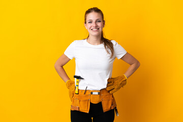 Young electrician woman isolated on yellow background posing with arms at hip and smiling