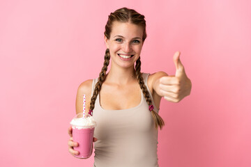 Young woman with strawberry milkshake isolated on pink background with thumbs up because something good has happened