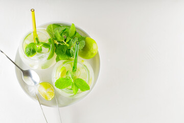 Mojito cocktail with lime and mint on a white background. Drink making tools and ingredients for cocktail. Two glasses of mojito on a white plate. Top view. Copy space
