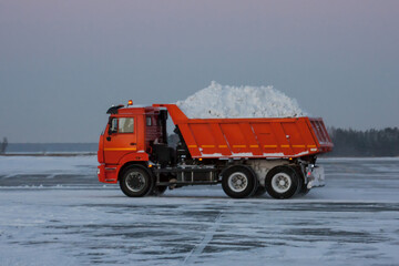Orange dump truck rides on a winter road with snow in the back body