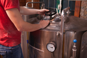 Unrecognizable brewer opening metal beer tank, working at microbrewery