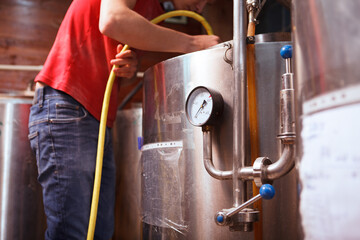 Selective focus on pressure gauge of beer tank, brewery technician washing inside the container with water hose