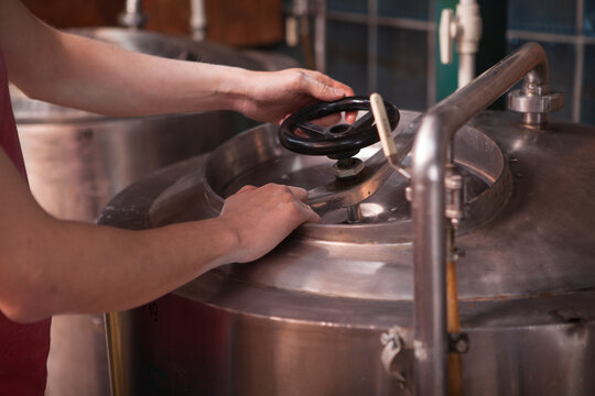 Cropped shot of a brewer opening metal beer tank, working at his brewery