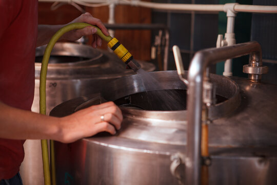 Cropped shot of a brewery technician washing beer tanks inside, using water hose