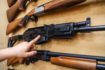 The buyer selects a firearm at a gun shop. Showcase with assortment of shotguns for hunting and...