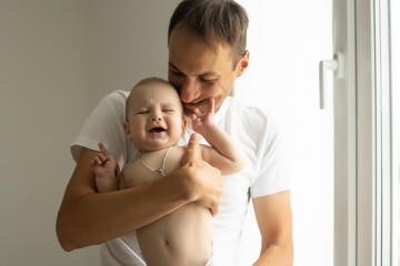 Father Hugging Newborn Baby in white bedroom.