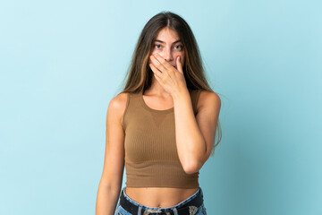 Young caucasian woman isolated on blue background covering mouth with hand