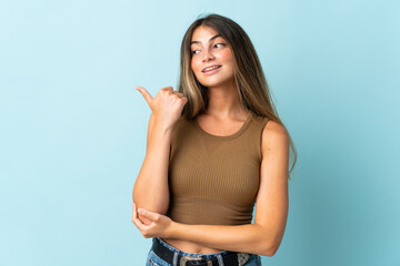 Young caucasian woman isolated on blue background pointing to the side to present a product