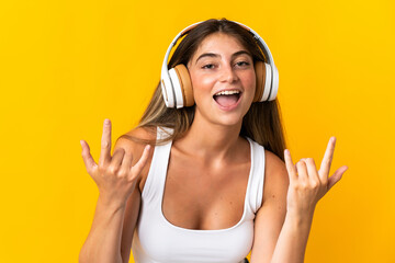 Fototapeta premium Young caucasian woman isolated on yellow background listening music making rock gesture