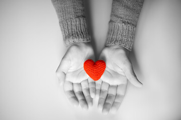 a person in a red sweater holds a red knitted heart in his palms. valentine's day holiday symbol....