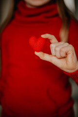 a person in a red sweater holds a red knitted heart in his palms. valentine's day holiday symbol