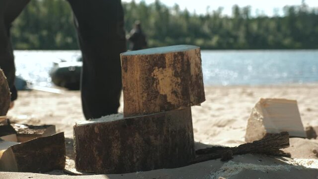 A man in nature on a sunny day cuts firewood with a large axe