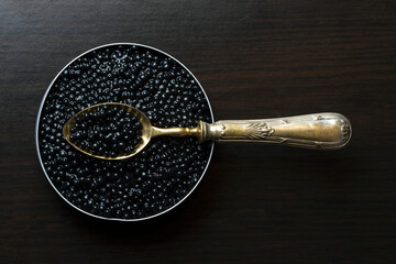 LUXURY GOLDEN SPOON IN BELUGA CAVIAR TIN CAN ON DARK WOODEN BACKGROUND. TOP VIEW. - obrazy, fototapety, plakaty
