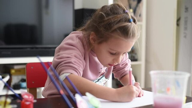 Small, beautiful girl in pink sweater draws of felt-tip pens. Child very likes drawing. Development of fine motor skills important in childhood. Creativity for children at home.