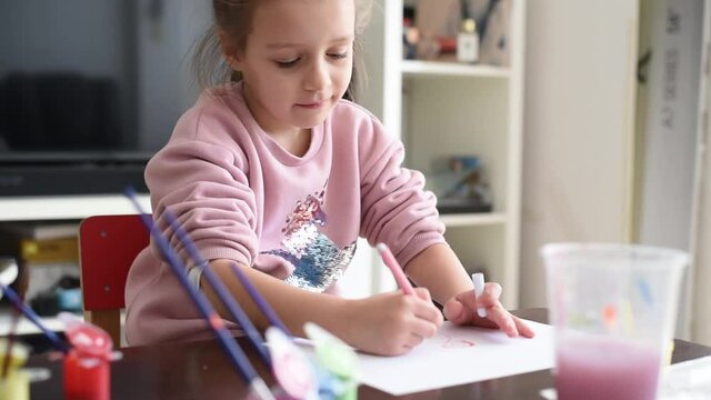 Small, beautiful girl in pink sweater draws of felt-tip pens. Happy child very likes drawing. Development of fine motor skills important in childhood. Creativity for children at home.