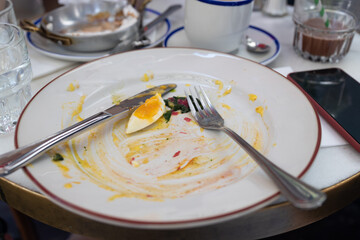 Empty dirty dish after breakfast with poached egg with tuna and cheese on toast, fork. White rustic trendy dirty plate on a table.