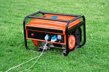 Portable electric generator with electric wires connected on the green grass in summer - obrazy, fototapety, plakaty