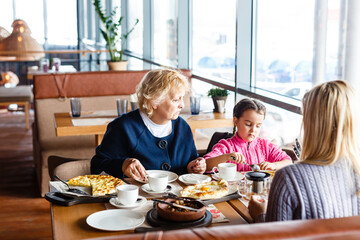childhood and people concept - happy grandmother and little girl with spoon eating at outdoor cafe or restaurant