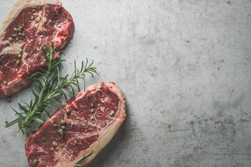 Raw beef steak background with salt and rosemary on grey concrete kitchen table. Preparing fresh...
