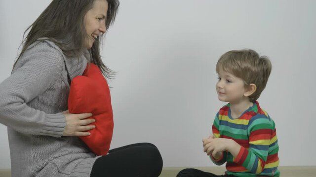Mother and son playing with big red heart pillow, love symbol