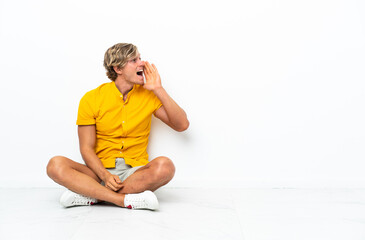 Fototapeta premium Young English man sitting on the floor shouting with mouth wide open to the side