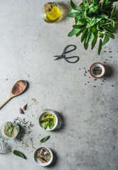 Food background with herbs, oil, salt , wooden spoon and other utensils on grey concrete kitchen table. Preparing homemade herbal salt with fresh ingredients. Top view.