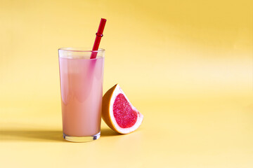 Grapefruit juice and a slice of grapefruit on a yellow kopi space background. Grapefruit juice in a glass glass with a red tube on a yellow background in natural light