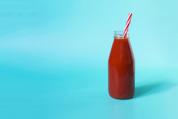 Tomato juice in a transparent bottle with a red plastic tube on a blue background - a place for text
