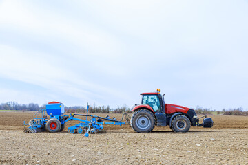 A tractor with a seeder in the field sows a large farmer's plantation with grain.
