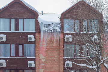 Huge dangerous icicles of ice hang from the roof of the house in winter or spring
