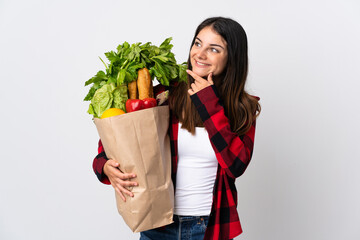 Young caucasian with vegetables isolated on white background looking up while smiling