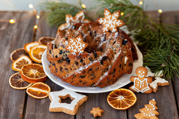 Traditional christmas sweet food: homemade cake with raisins, nuts, fruits decorated with gingerbread cookies. Wooden background, fir tree branches, fairy lights