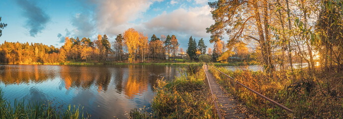 Beautiful wide angle panorama of October landscape with lake, colorful trees, metal bridge,  clouds and blue sky
