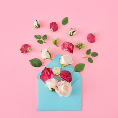 Creative composition made of spring flowers and leaves on pastel pink background and paper envelope. Nature bloom idea. Minimal spring concept, flat lay, top view.
