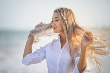 A girl with long hair in a bluish swimsuit and a shirt goes through her hair on the seashore