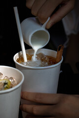 a hand of a young woman hold a cup of milk pouring into a paper coffee cup