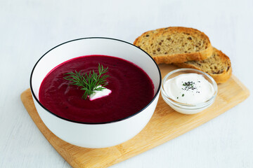 homemade red vegetable soup with greens on the cutting board. white bowl of Beetroot cream soup...
