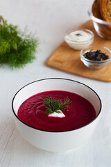 red beet soup.homemade red vegetable soup with greens. white bowl of Beetroot cream soup with bread and spices on a white background. Healthy diet lunch with copy space. vertical