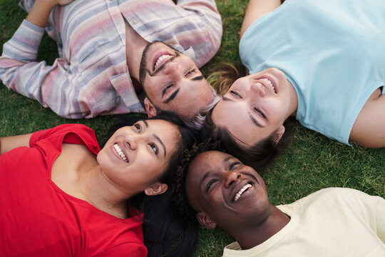 Young friends smiling lying together on grass in park. Focus on Latin American Girl