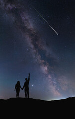 Fototapeta premium A couple of people in love hold hands and look at a shooting star at night against the backdrop of the Milky Way. The silhouettes are drawn by hand without a reference image. 