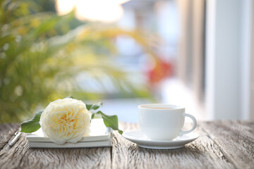 White tea cup and rose flower and notebook on wooden table