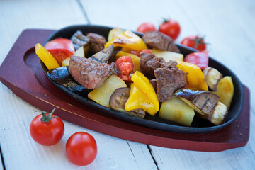 Pieces of meat with vegetables are on a platter. Along with the meat, pears, sweet peppers and eggplants. Decorated with cherry tomatoes. The concept of recipes from the restaurant