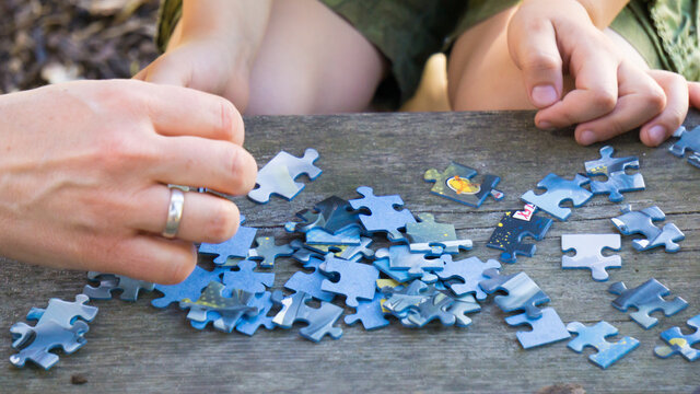 A hand reaching for a piece of a puzzle scattered on a wooden floor