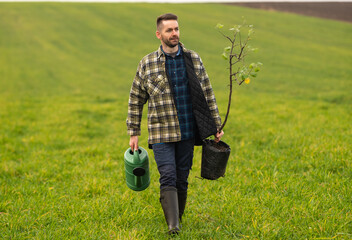 The handsome man is going to plant a tree in the field - obrazy, fototapety, plakaty