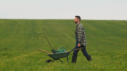 The handsome gardener walking with a wheelbarrow through the field